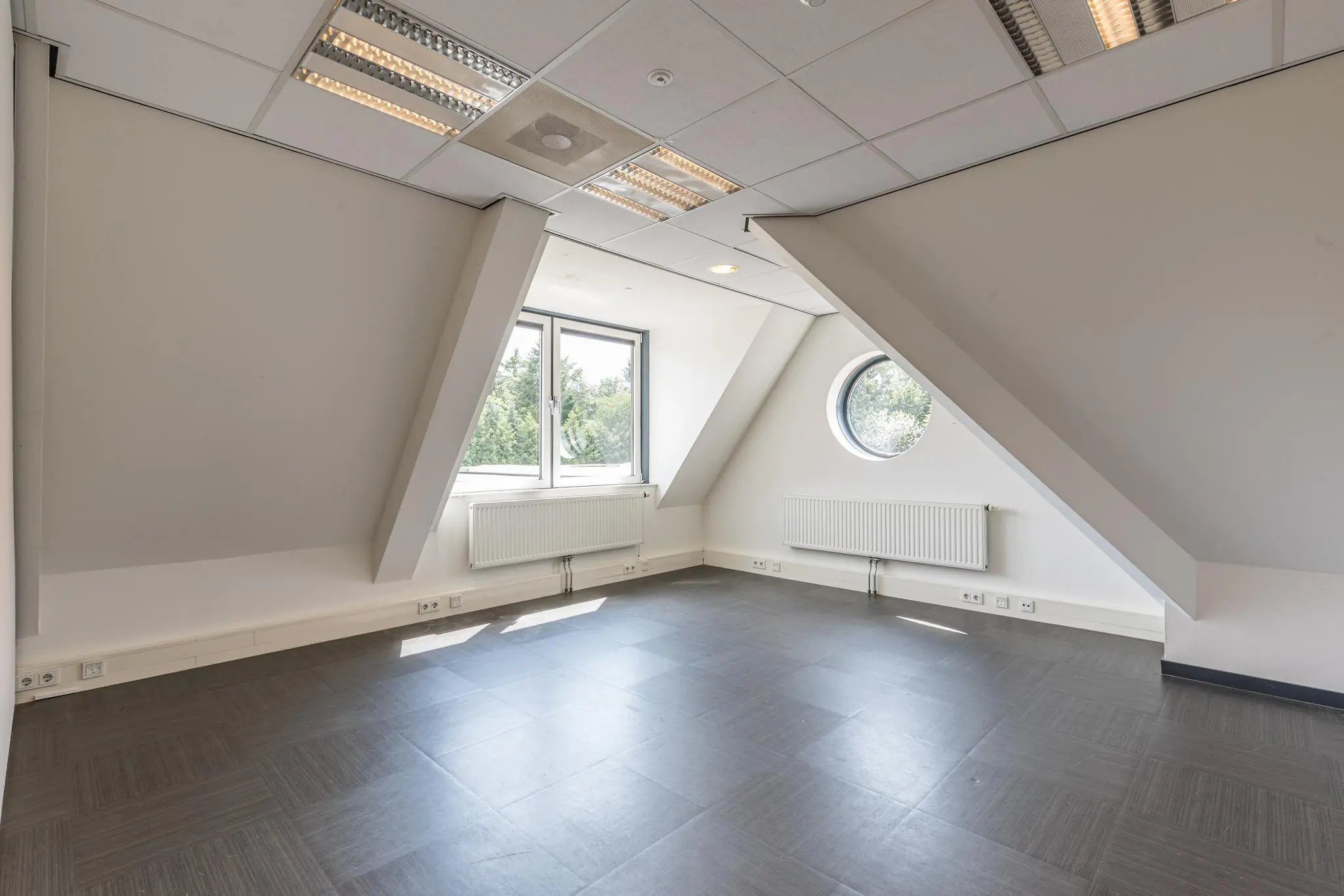 Lichte, lege kantoorruimte aan de Laan Blusse van Oud-Alblas met schuin dak, een rechthoekig en rond raam.